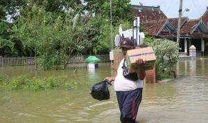 Foto : Sunardi sedang Memikul Bahan Pokok di Tengah akses jalan Desa Karangrowo yang tergenang Banjir. (Dok. Mitrapost.com/Ilham)