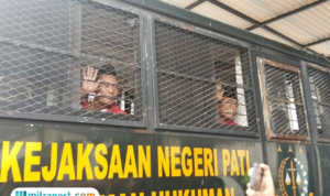 Foto : Supriyono alias Botok melambaikan tangan di dalam truk tahanan Kejaksaan Negeri Pati, Rabu (24/12/2025). (Sumber. Mitrapost.com/ Ilham)