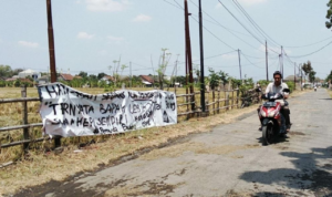 Foto : Jalan Rusak Dipasangi Spanduk di Desa Bumirejo Kecamatan Margorejo. (Sumber. Mitrapoat.com/ Ilham)