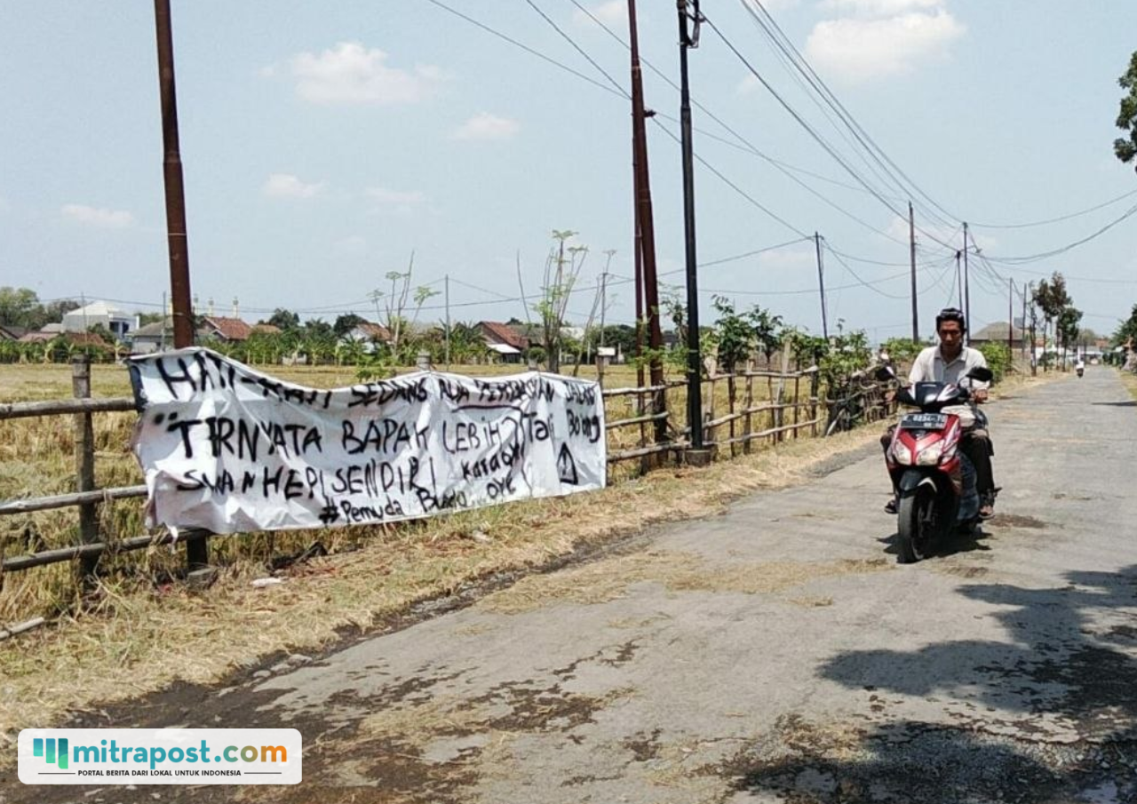 Foto : Jalan Rusak Dipasangi Spanduk di Desa Bumirejo Kecamatan Margorejo. (Sumber. Mitrapoat.com/ Ilham)